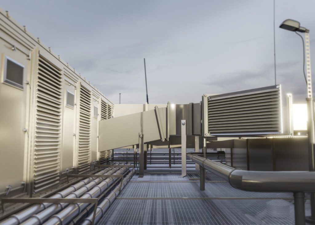 Industrial rooftop with HVAC units, ductwork, and ventilation systems, featuring metal grates and conduits under a cloudy sky.