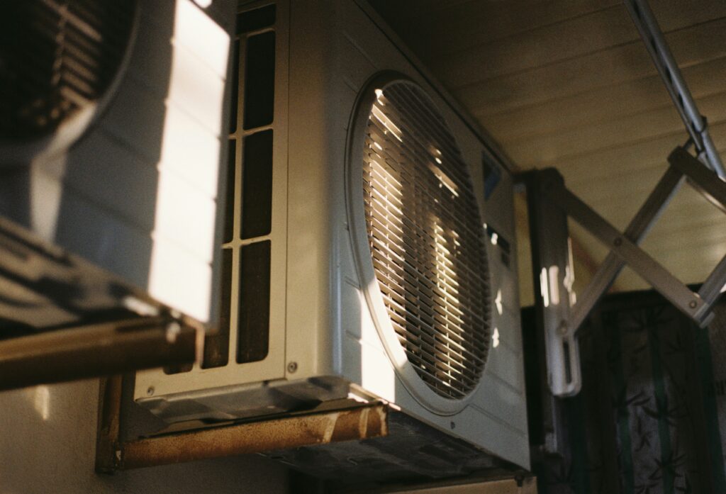 Close-up view of an outdoor air conditioning unit mounted on a wall, partially illuminated by sunlight.